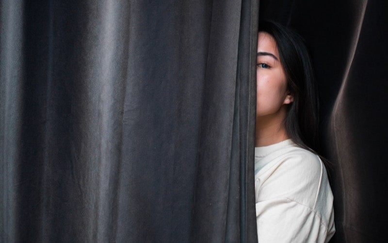 woman hides her face behind a curtain