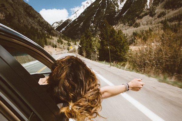 girl holds head out of a car window during road trip