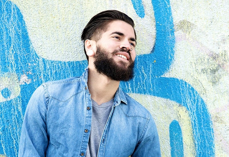 Smiling pierced man leaning on wall with graffiti art