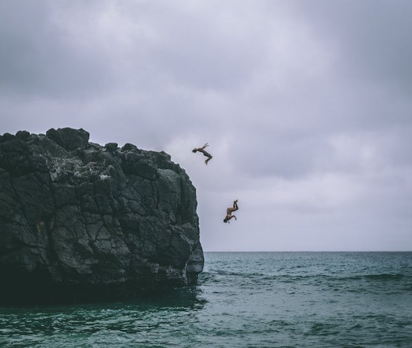 two people jump into the ocean from a cliff