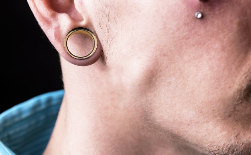 Man with stretched ear lobes wearing gold tunnel plugs
