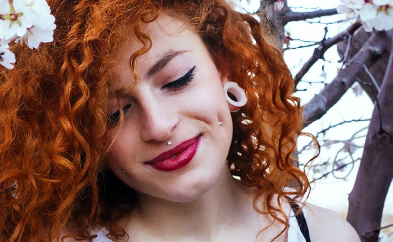 Red haired woman with stretched ears and facial piercings.